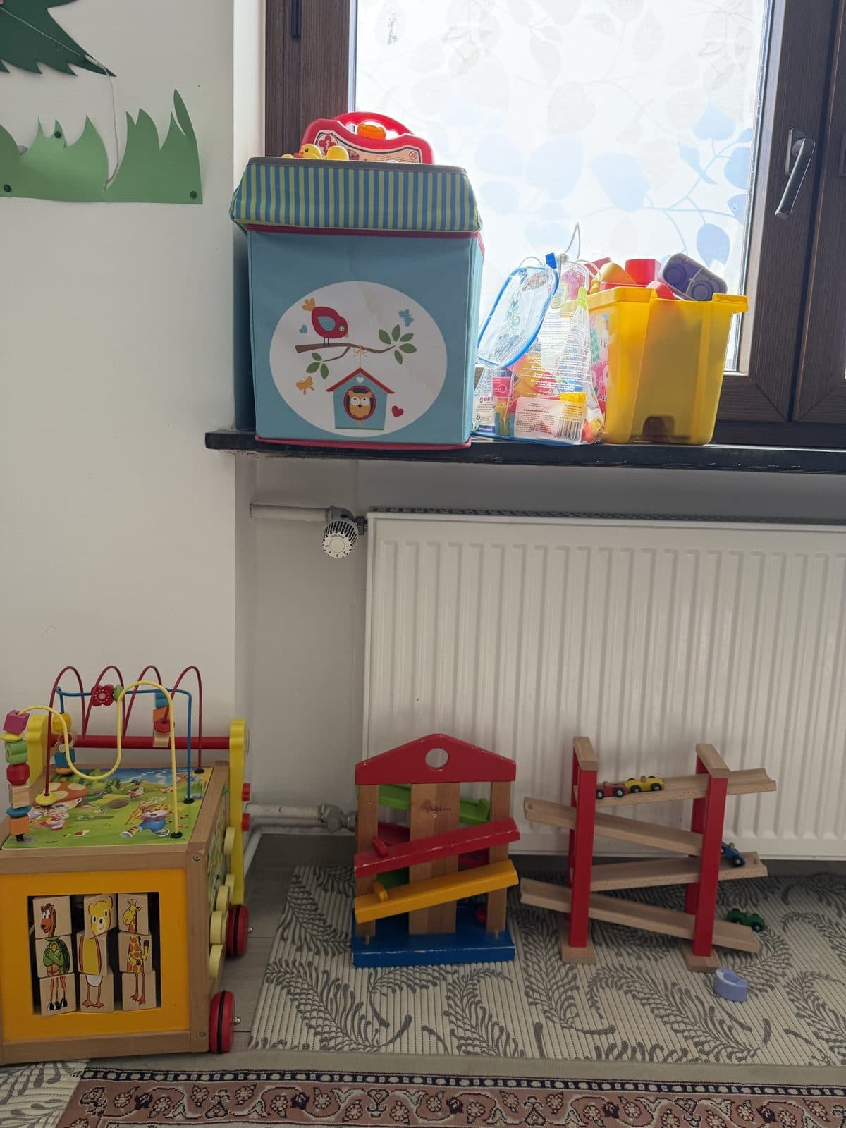 Spielecke mit Holzspielzeug, Kugelbahnen und Lauflernwagen am Fenster